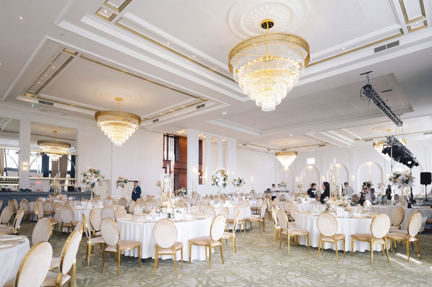 Elegant ballroom with crystal chandeliers, white linens, and gold chairs set up for a luxurious wedding reception.