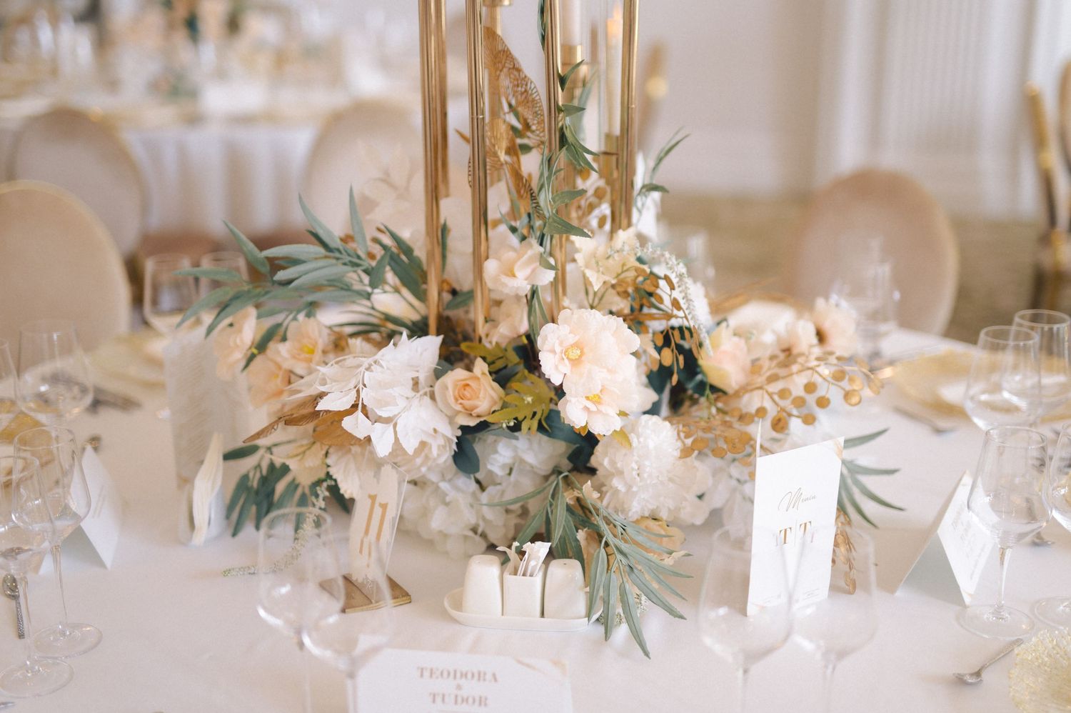 Elegant wedding centerpiece with blush roses, eucalyptus leaves and gold candlesticks on white tablecloth.