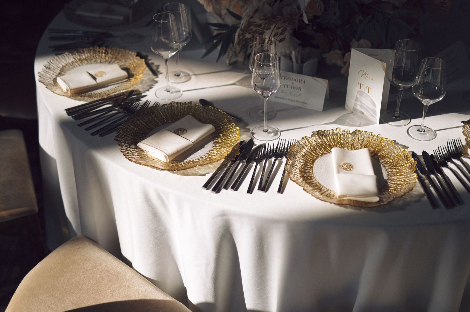 An elegant table setting with white linens, gold charger plates, and formal place settings for a special occasion.