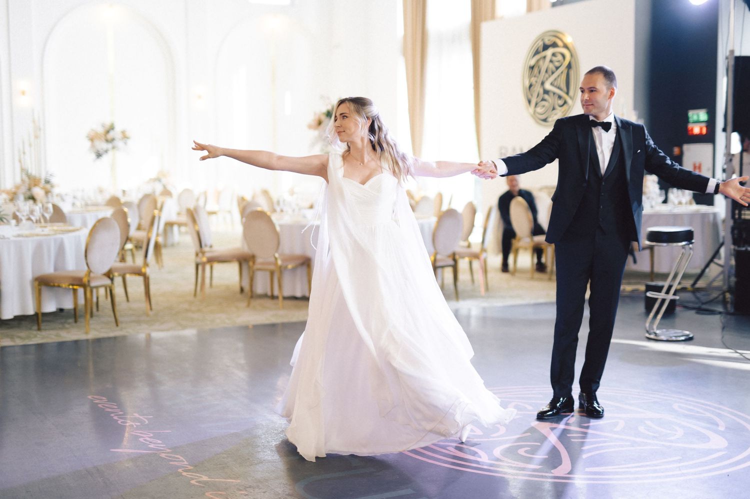 A wedding couple performs their first dance in an elegant white ballroom while spinning and twirling gracefully.