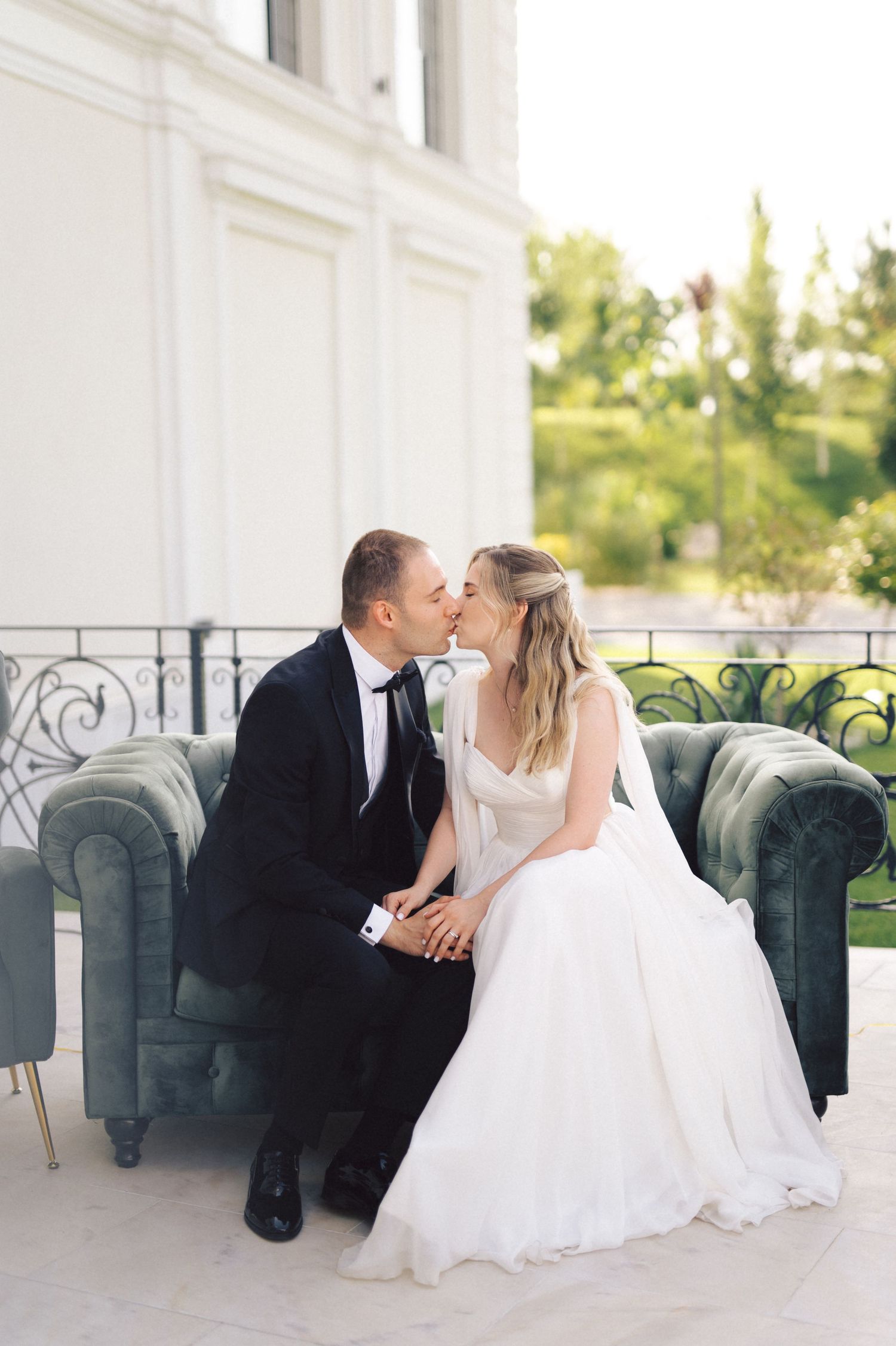 Romantic wedding couple shares intimate moments while sitting together on an elegant blue velvet couch on their special day.