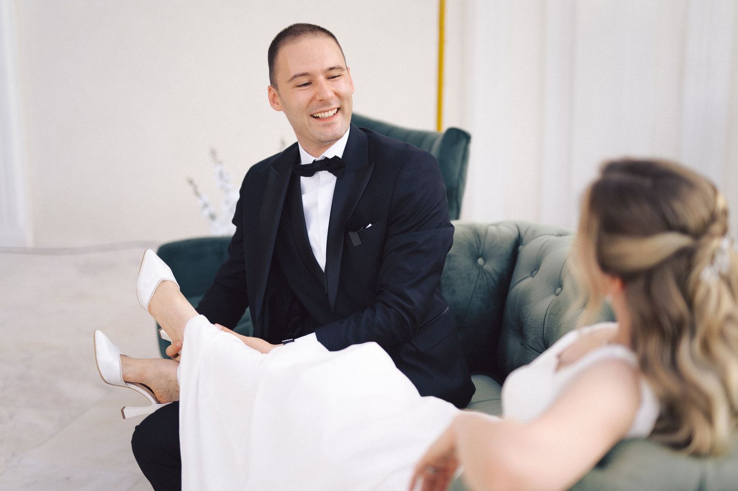 A couple shares a joyful moment on a teal couch during their wedding celebration.