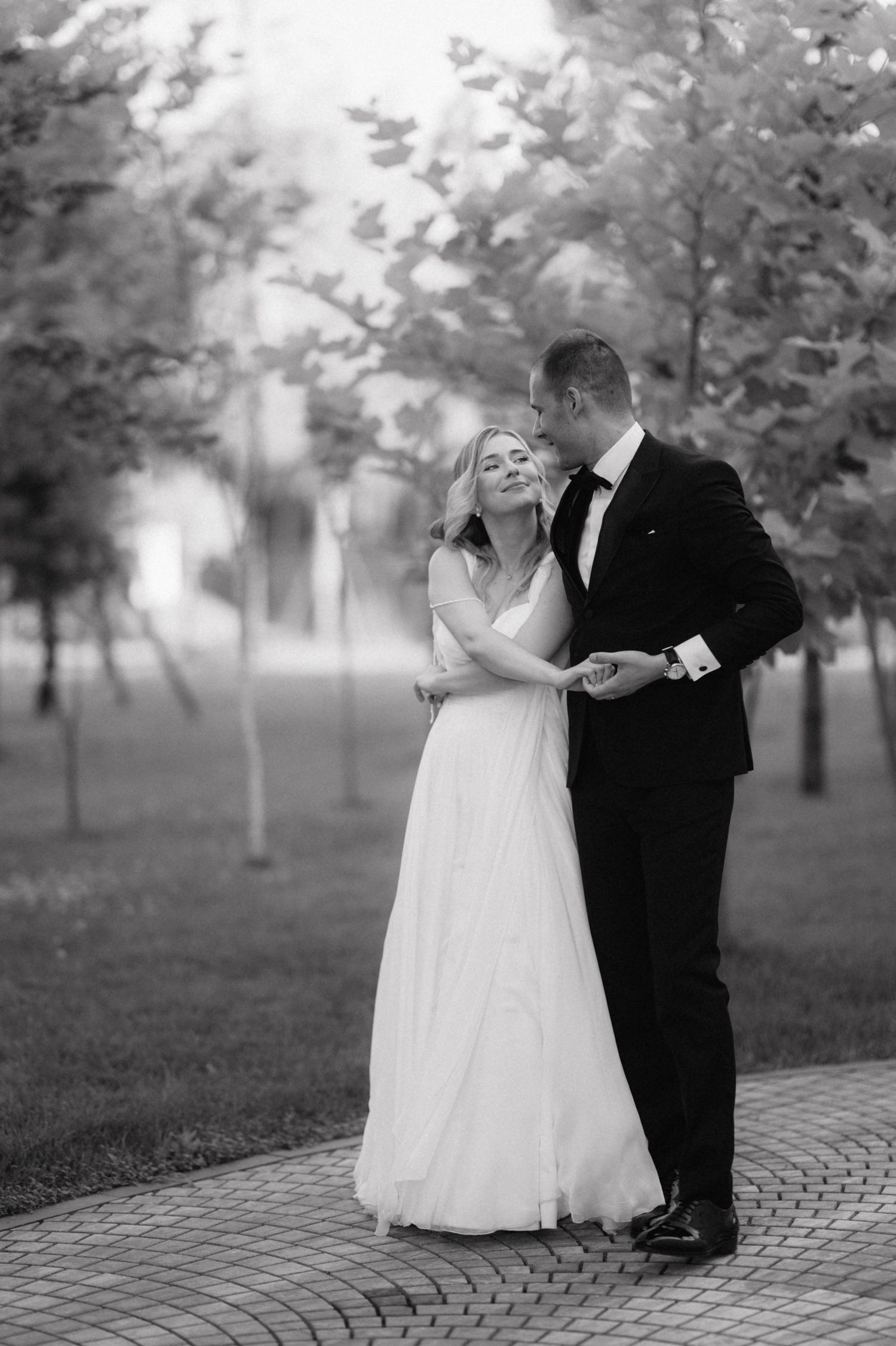 A romantic black and white wedding photograph sequence showing a couple dancing together in a park setting.