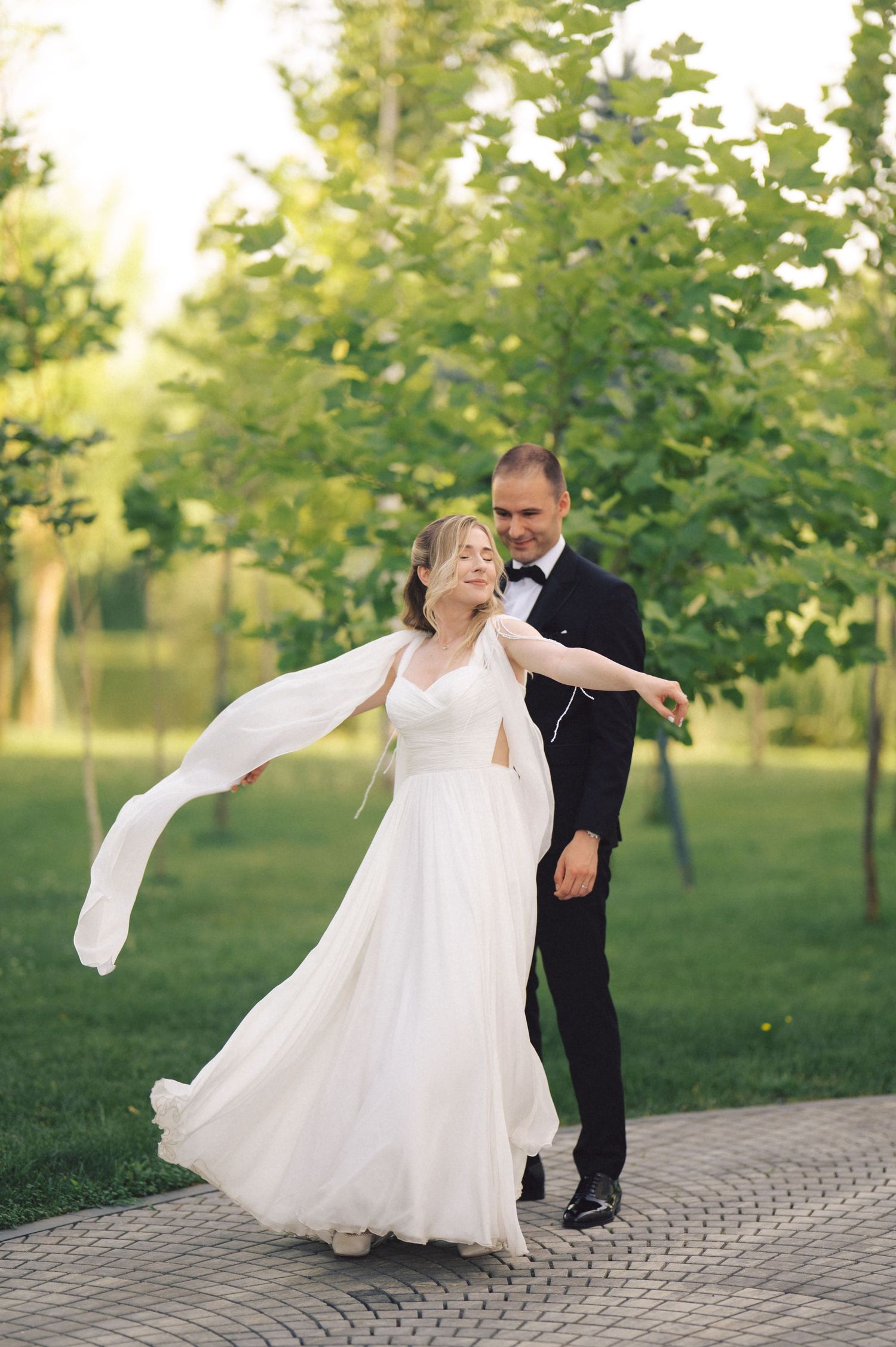 A romantic sequence of wedding dance photos showing a couple twirling on a brick pathway in a lush green park setting.