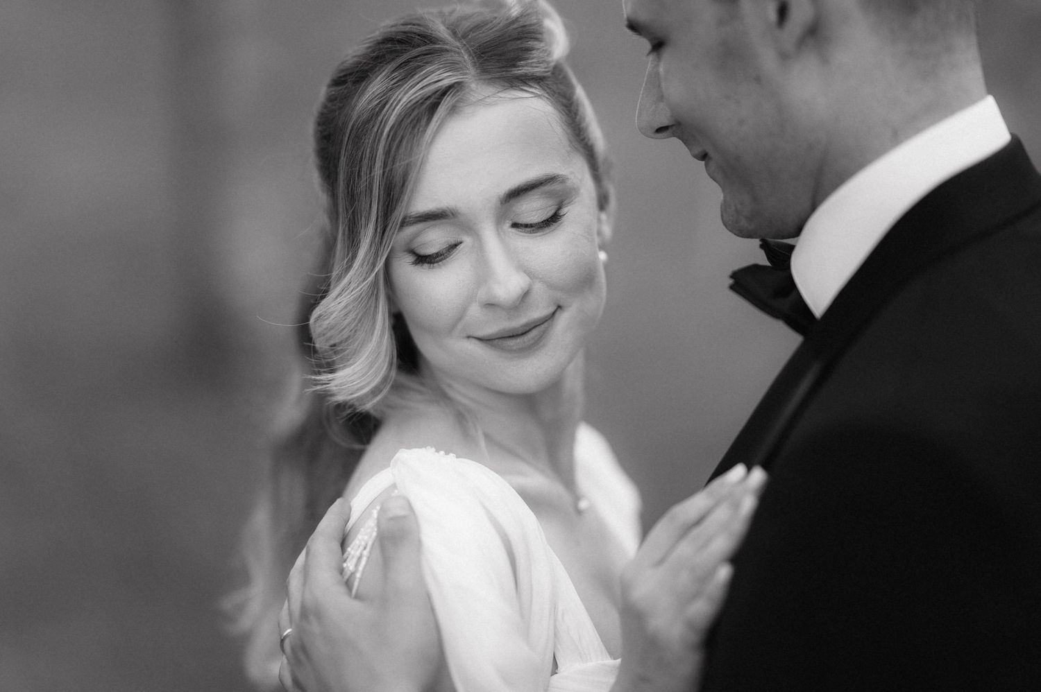 Black and white portrait of a tender moment between bride and groom with soft lighting and elegant formal attire.