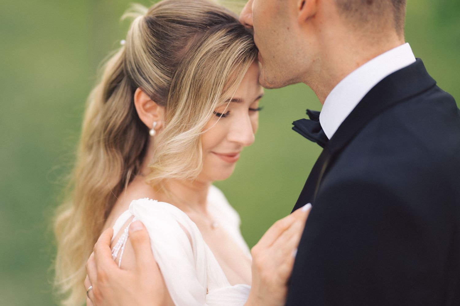Close-up wedding photos showing tender moments between a couple in formal attire against a natural outdoor backdrop.