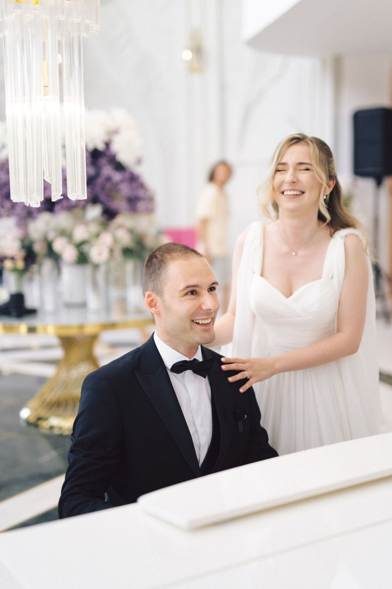 Elegant couple shares playful moments at wedding reception with crystal chandelier decor.