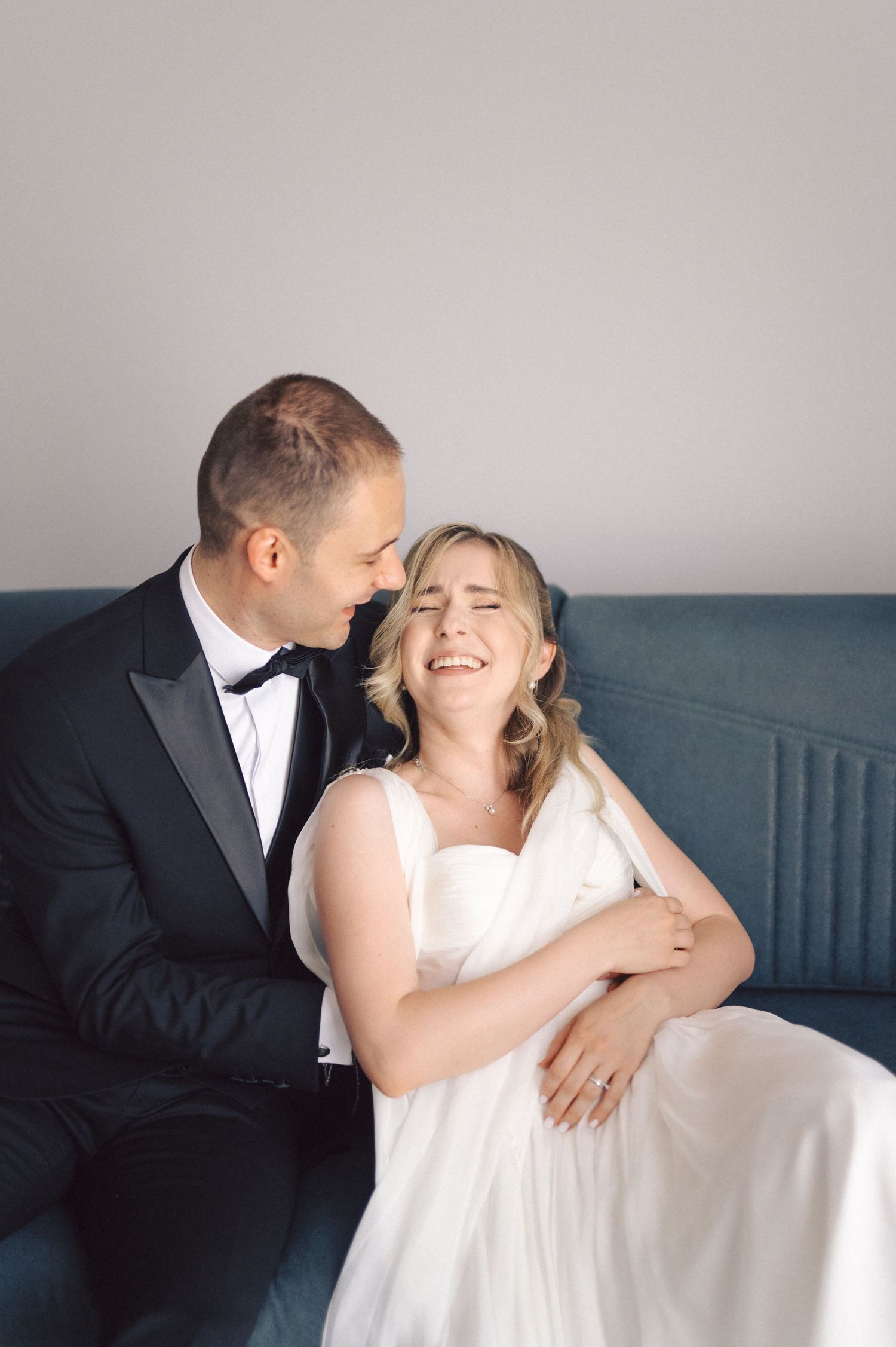 Intimate wedding portrait on blue couch shows tender embrace in natural light.