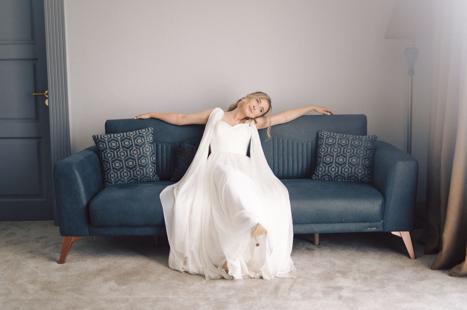 Wedding dress flows gracefully across blue couch in minimalist room setting.