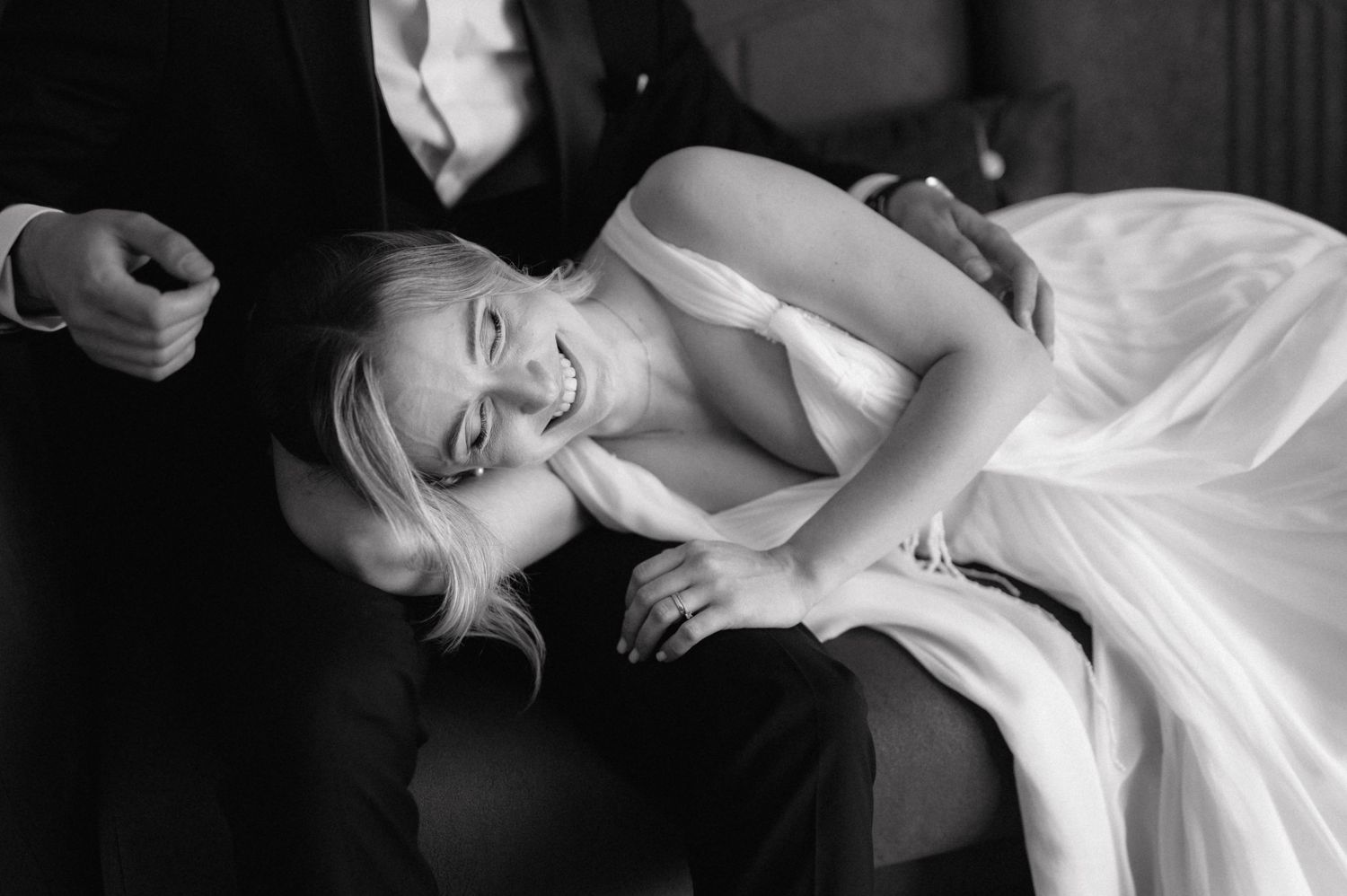 Black and white photo of someone in a white gown laughing joyfully while laying down.