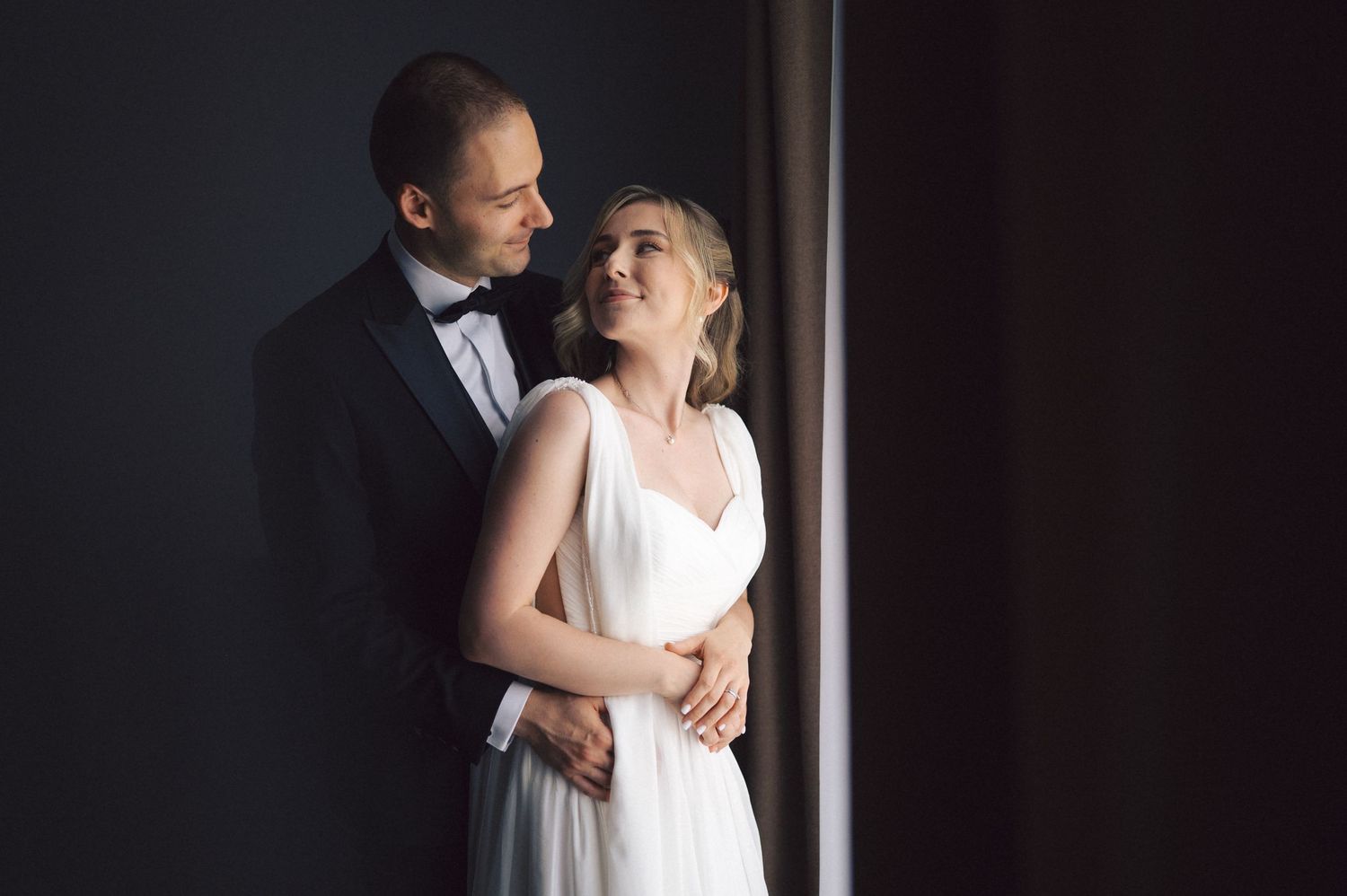Intimate moment captured of a couple in formal attire standing in moody lighting.