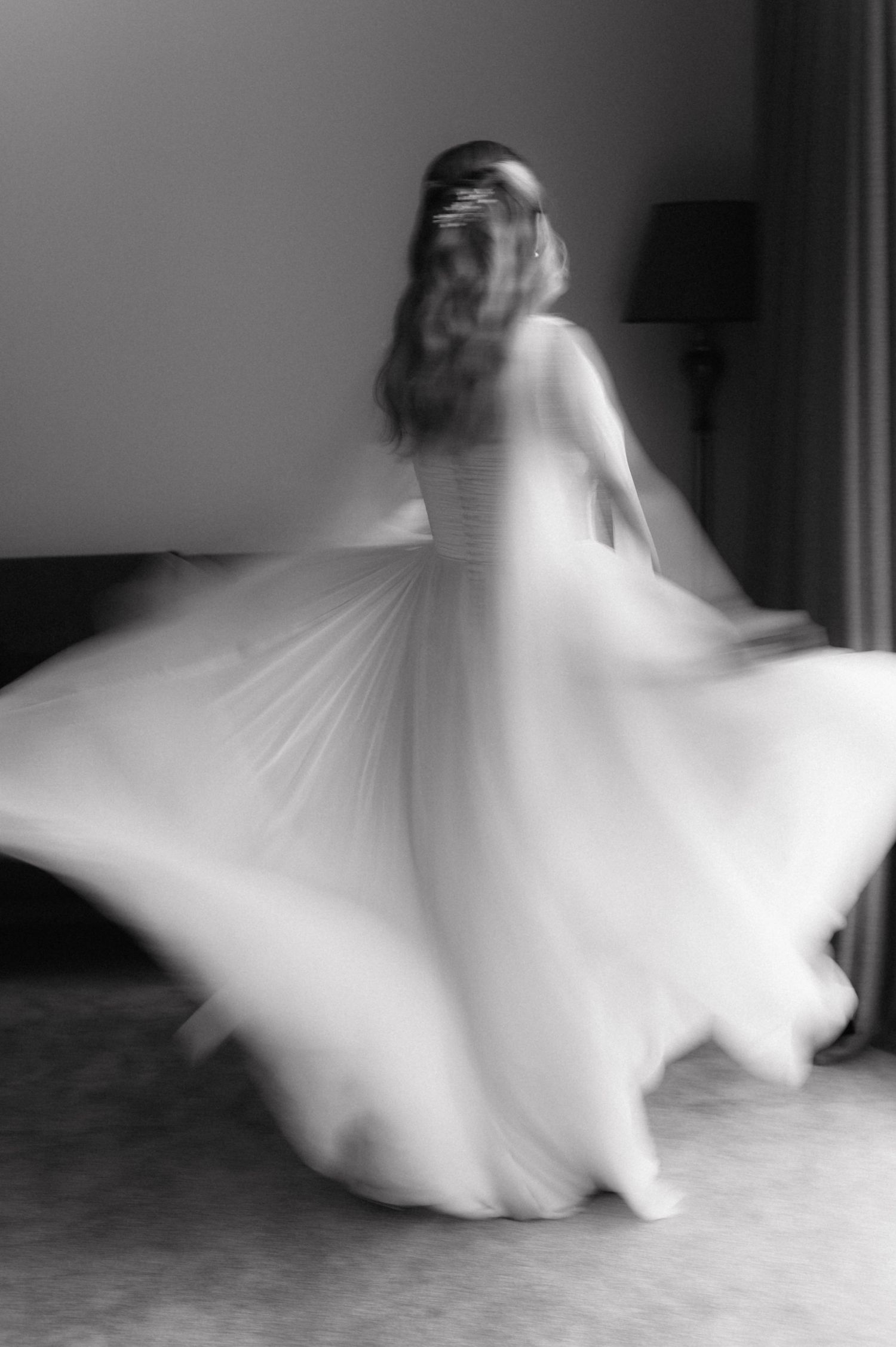 A twirling bride in a flowing white dress creates a dreamy motion blur effect in black and white photography.