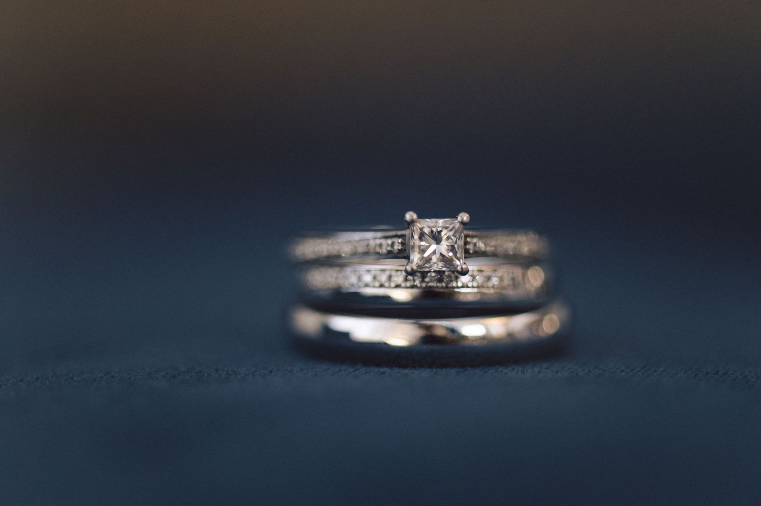 Close-up of diamond engagement ring and wedding band set against a dark blue background.