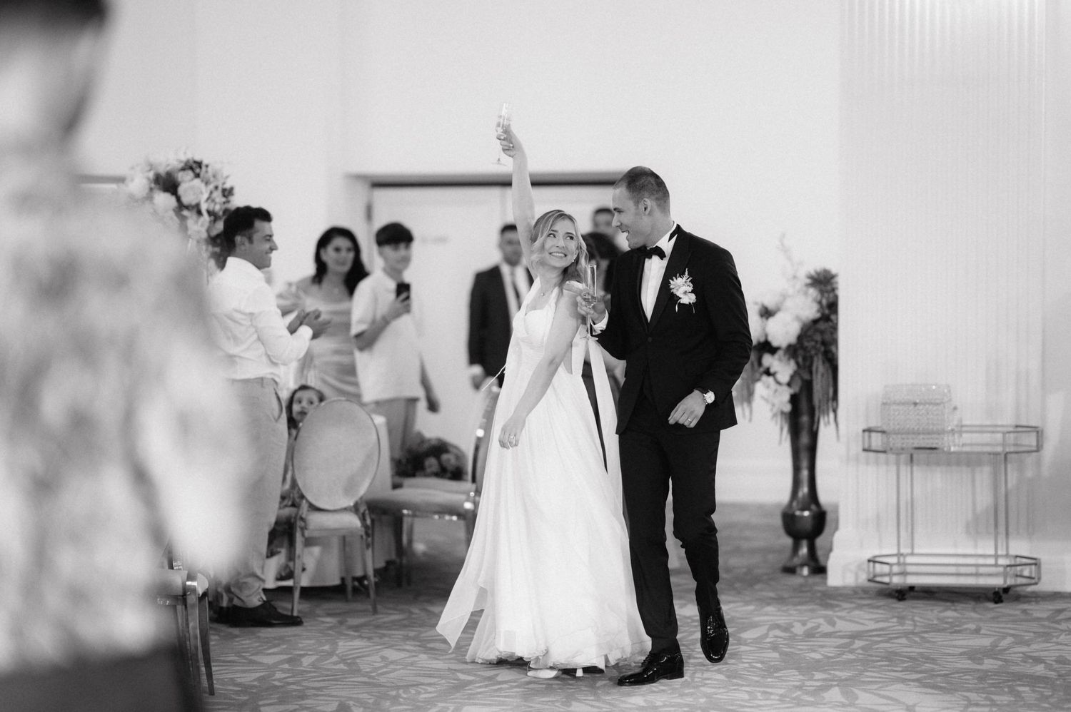 Black and white photo of newlyweds celebrating with guests during wedding reception.
