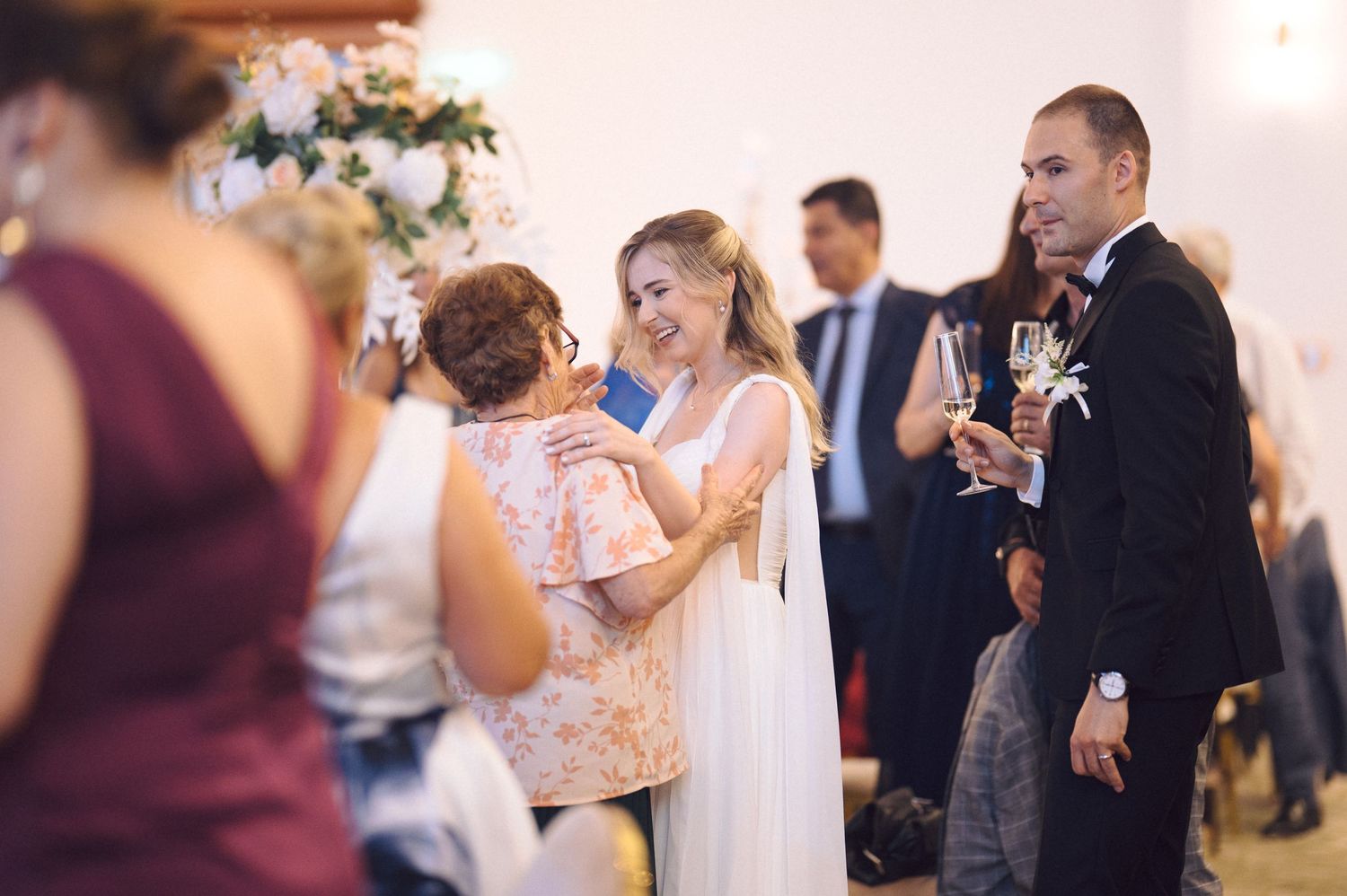 Wedding attendees dancing and socializing during a reception celebration with white decor and soft lighting.
