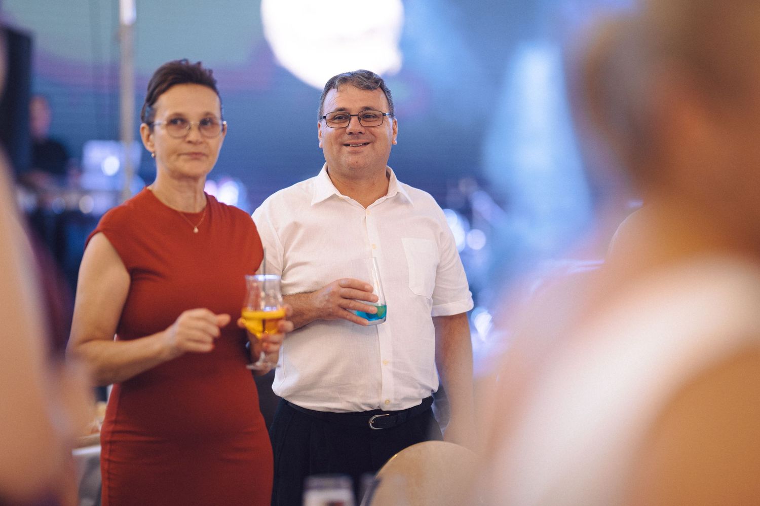 People enjoying drinks and conversation at an elegant social gathering with festive lighting and blurred backgrounds.