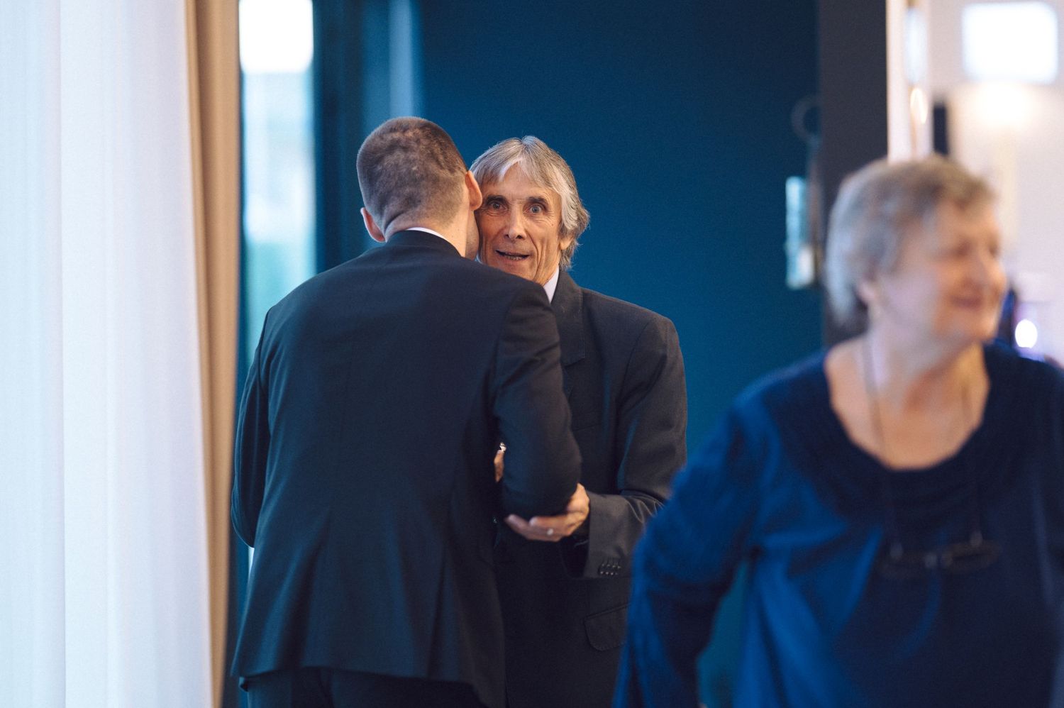 Candid wedding moments captured in moody blue lighting showing guests interacting at a reception.