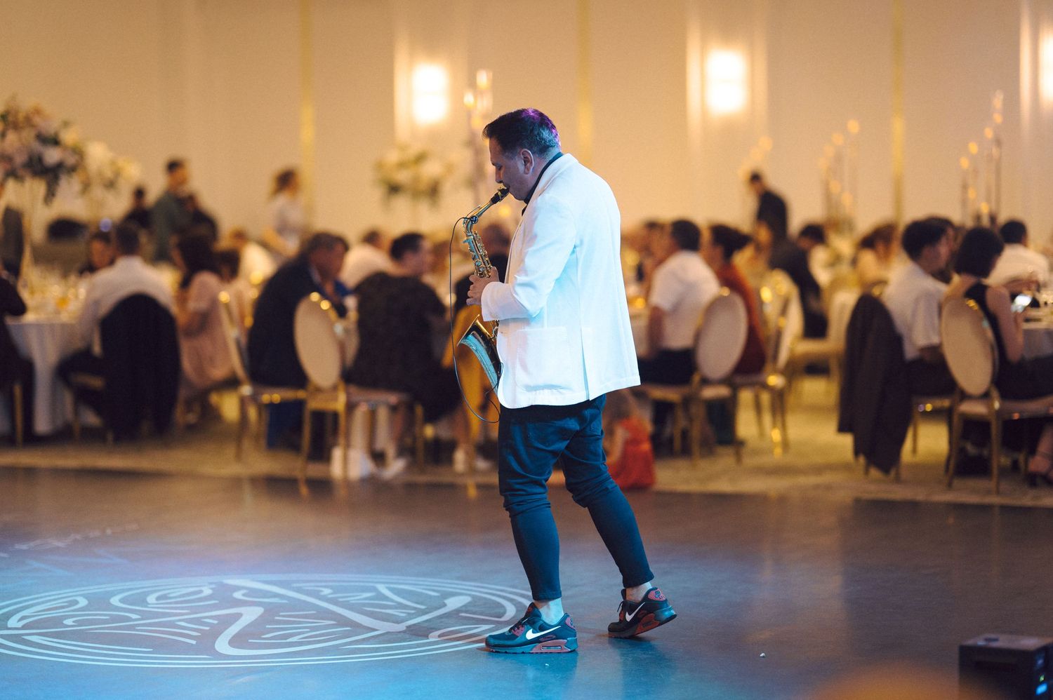 A person performing dance movements across a large indoor studio floor with other people in the background.