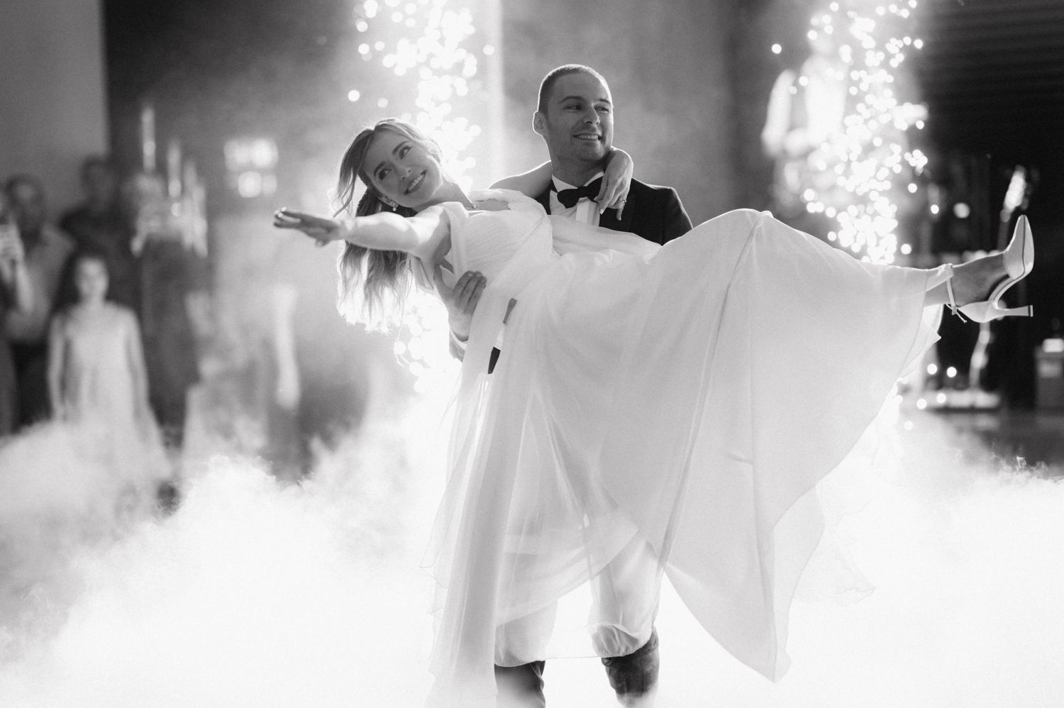 A couple performs an elegant first wedding dance surrounded by fog and sparklers in black and white.