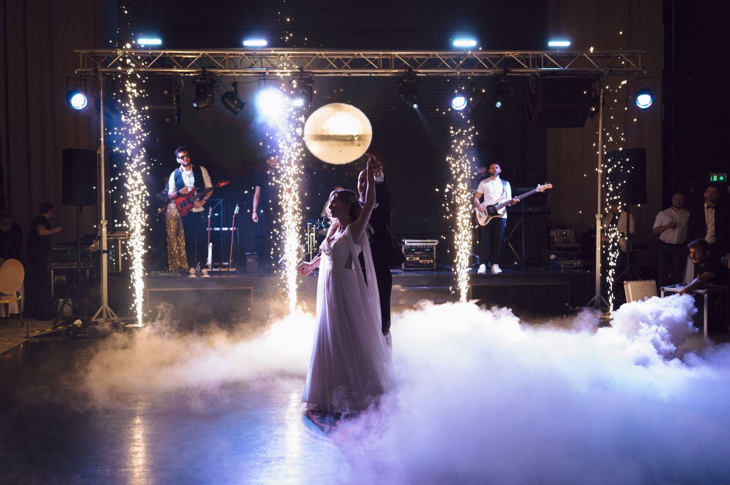 A couple dances surrounded by low lying fog and sparkling lights on a dark dance floor at a wedding reception.