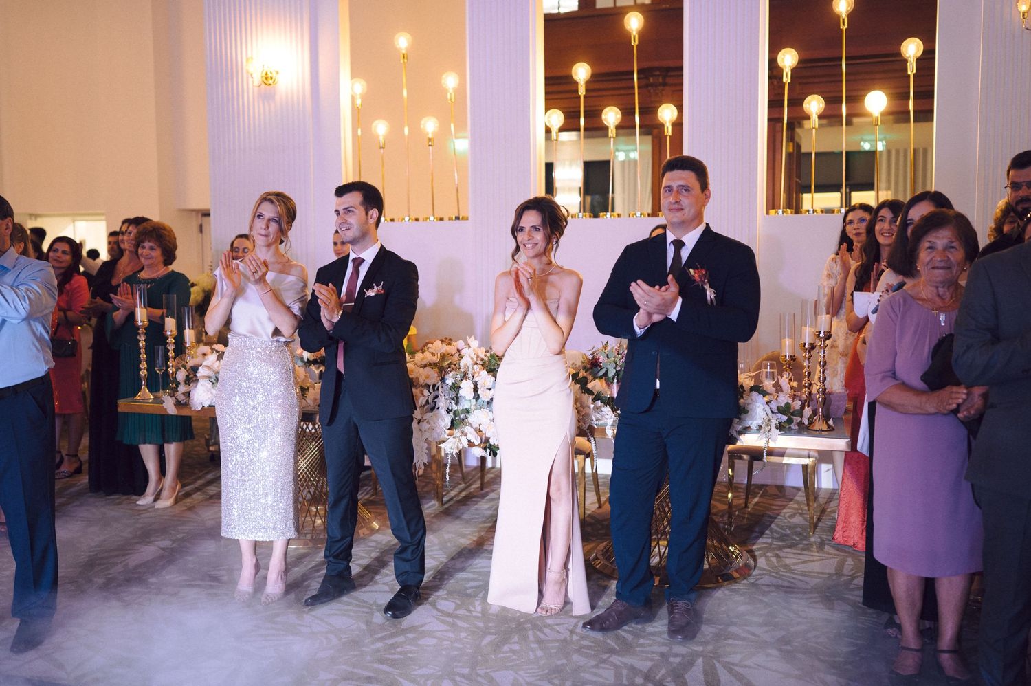 A panoramic view of wedding guests dancing and mingling in an elegant reception hall with warm lighting.