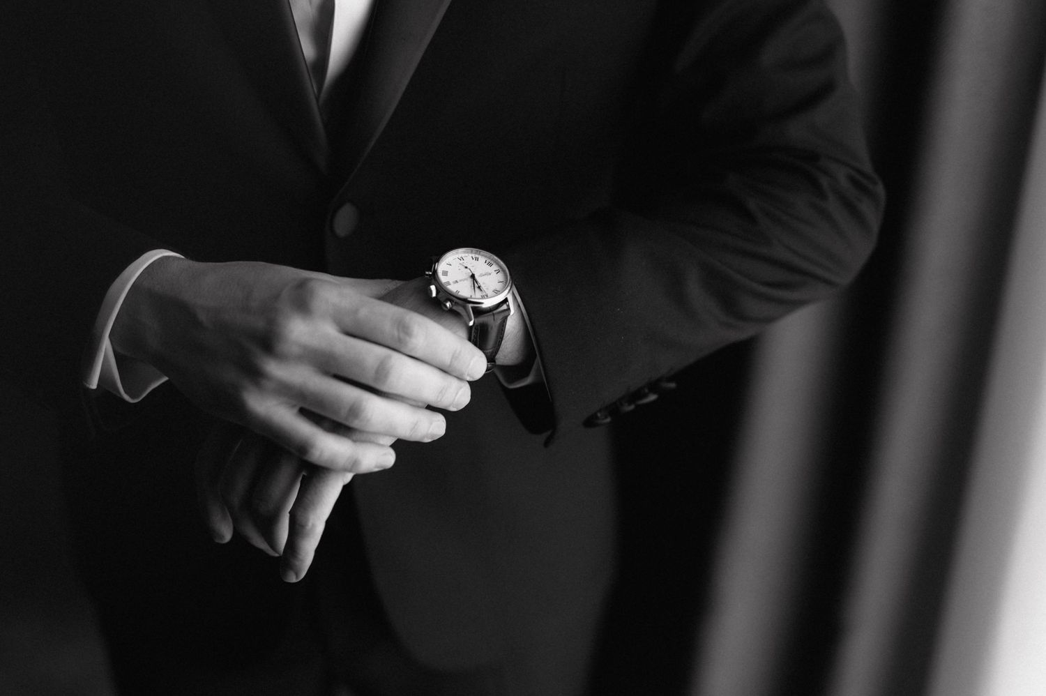 A close-up black and white shot of hands adjusting a wristwatch while wearing formal attire.