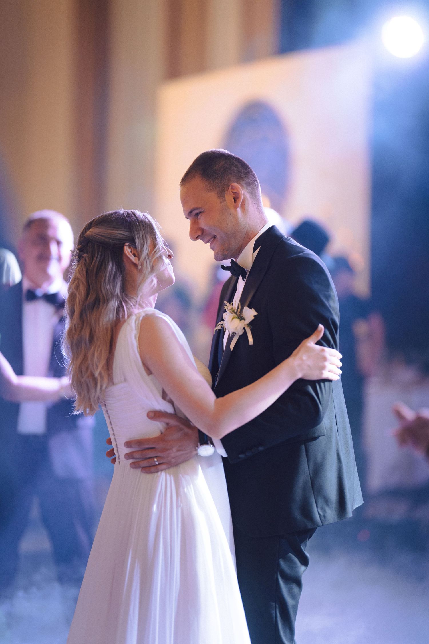 Couple shares romantic first dance at wedding reception with atmospheric lighting and fog on dance floor.