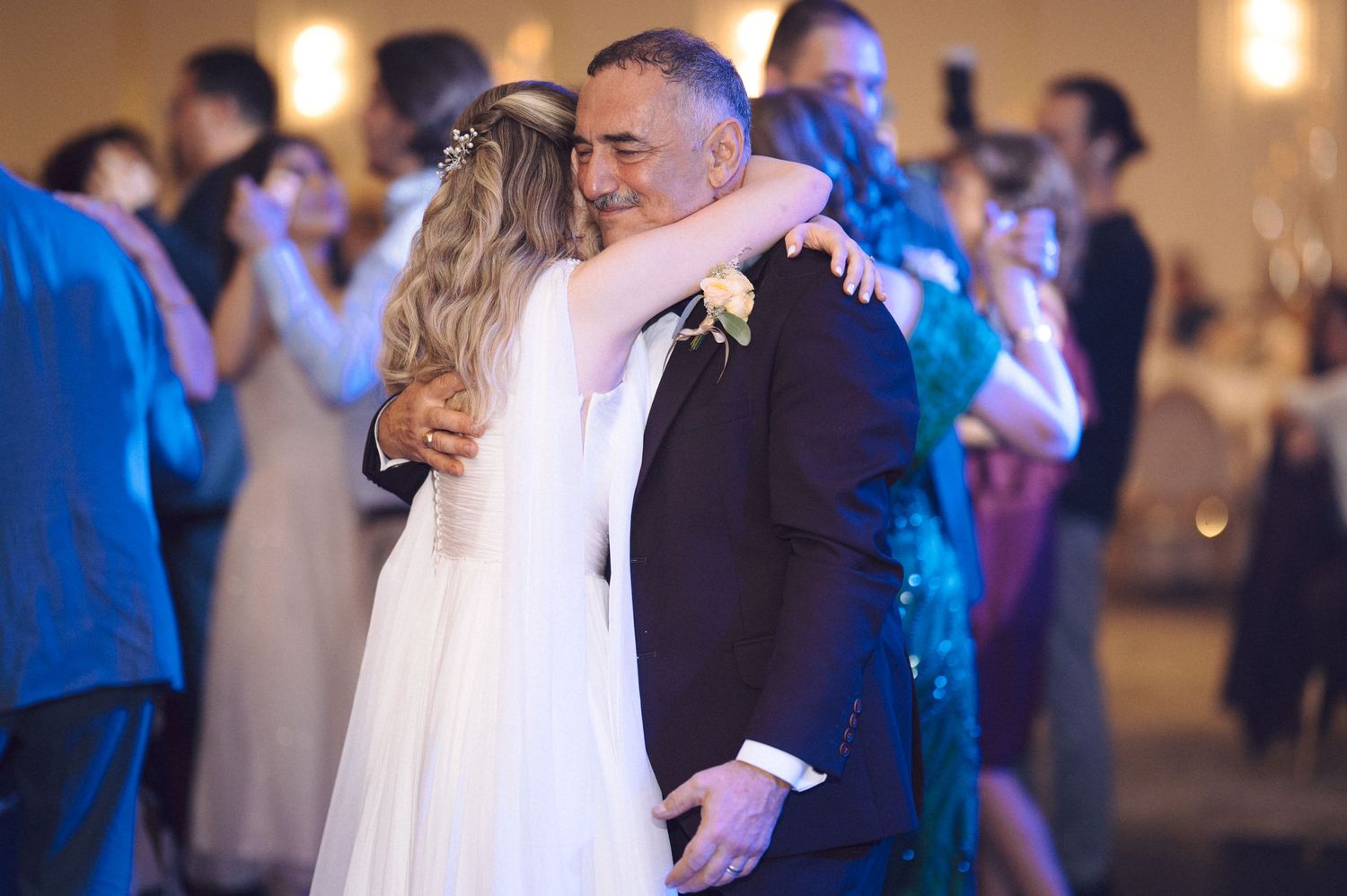 A couple shares an intimate moment during their first dance at a wedding reception in an elegantly lit ballroom.