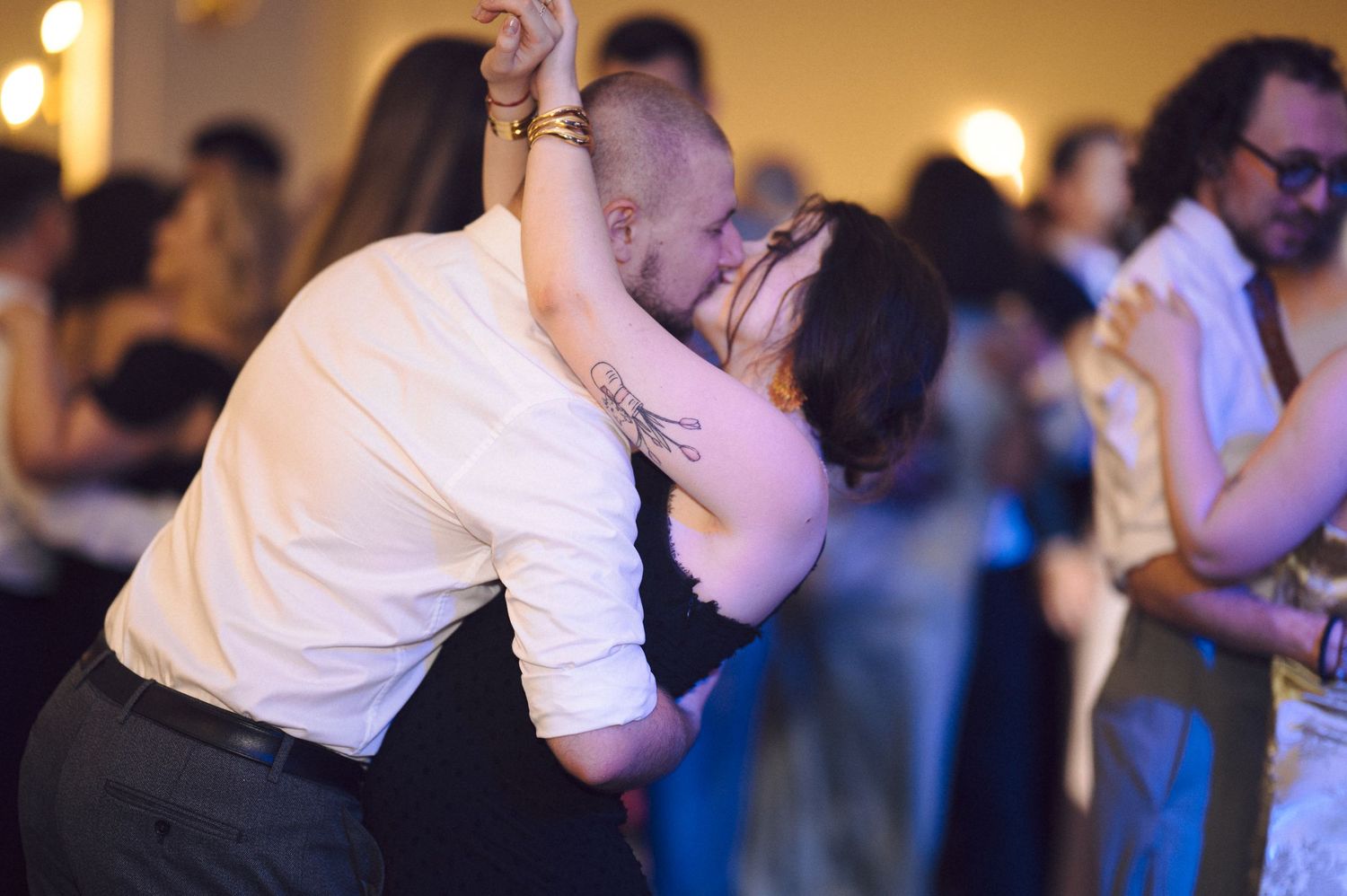 Two dancers share an intimate moment during a dance while other couples twirl in the background at a formal event.