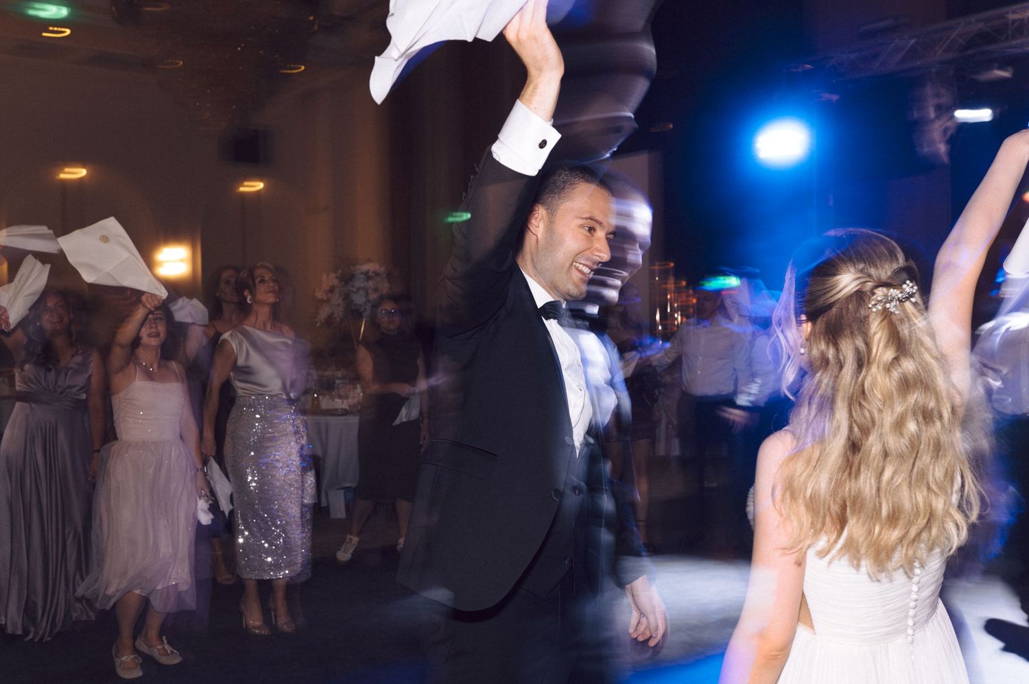 Wedding guests dance and celebrate on a dimly lit dance floor with blue lighting and disco effects.