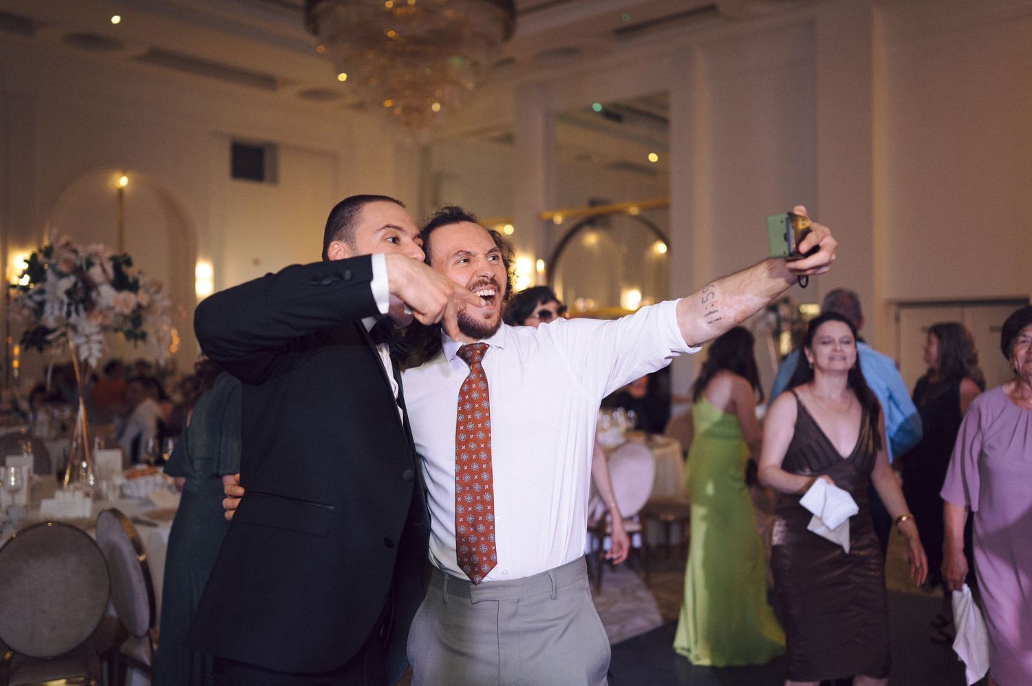 People dancing and celebrating in a banquet hall during a formal event with mood lighting.