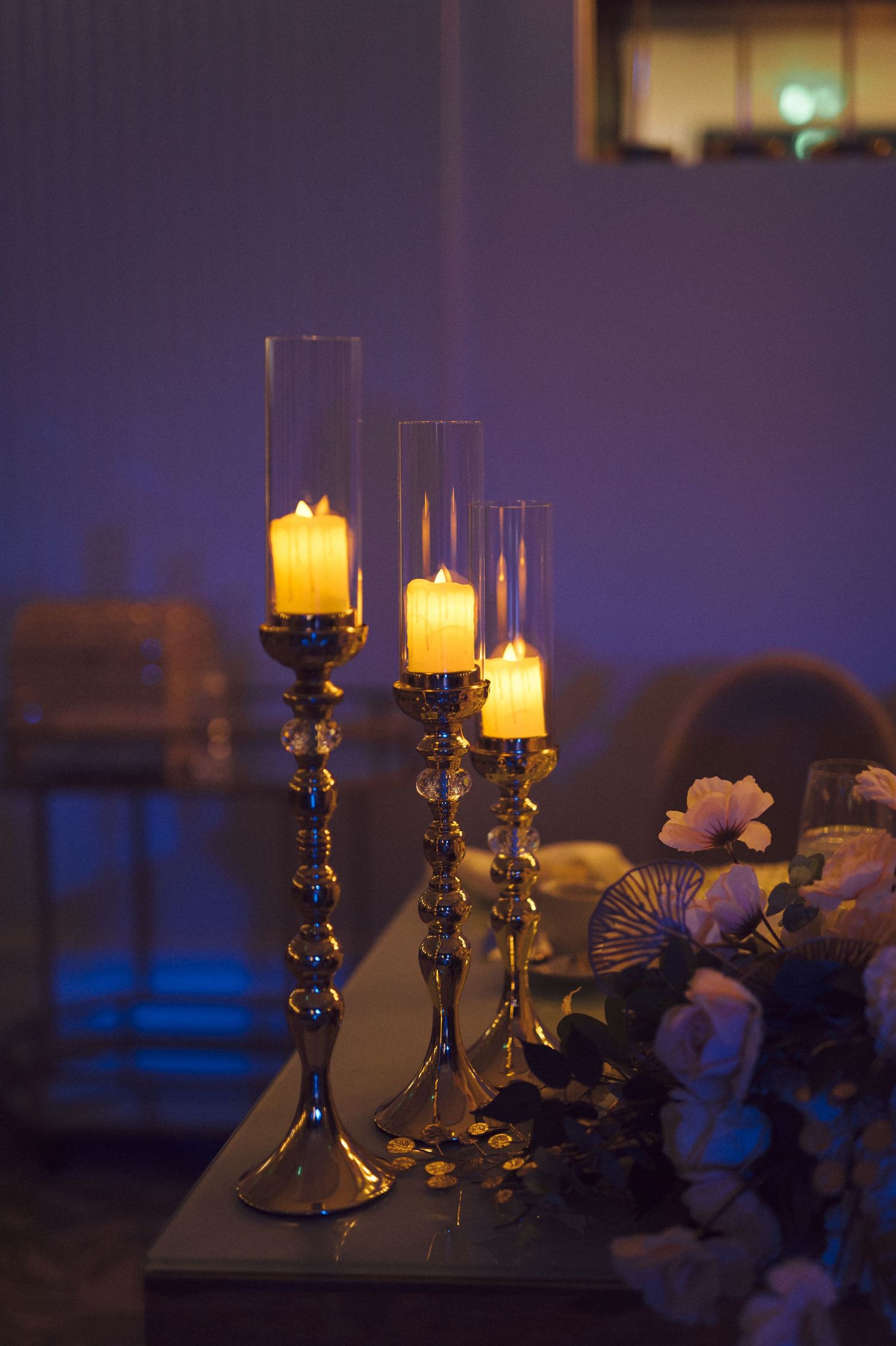 Three elegant candlesticks with glowing candles and glass hurricane shades set against a moody purple background.