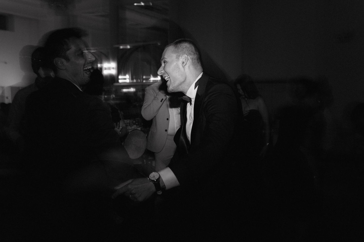 Black and white photo of people talking at a dimly lit party or event.