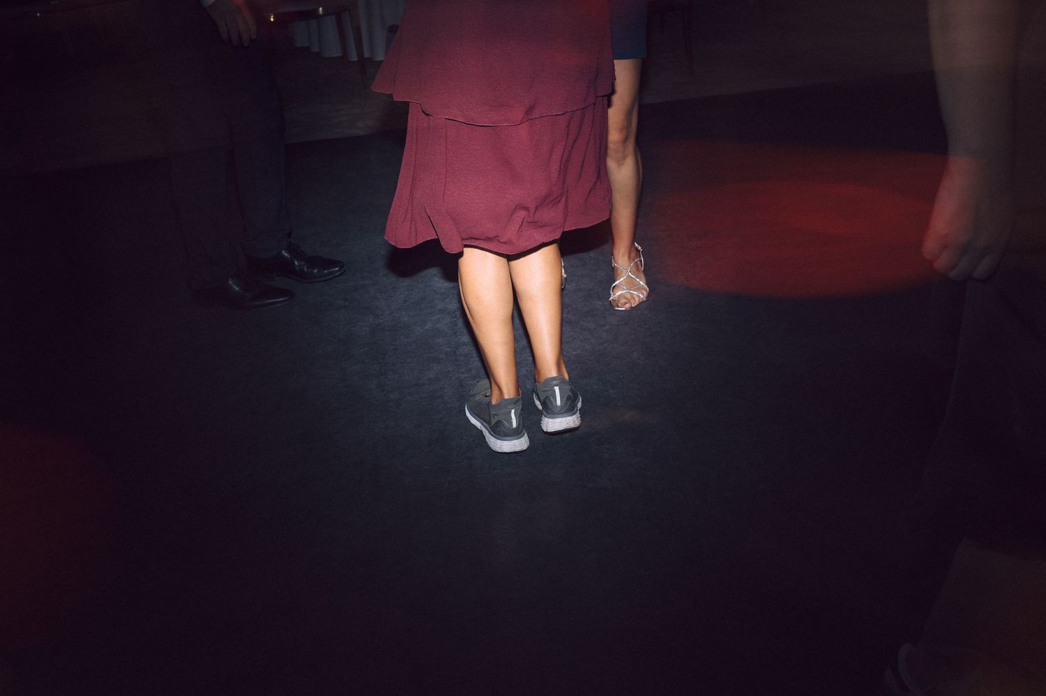 Feet in blue sneakers and a red dress visible in a dimly lit room.