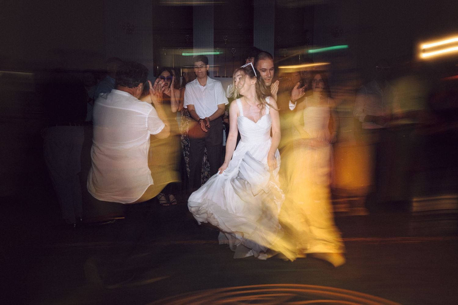 Motion-blurred photo of a reception dance floor with a bride in white dress spinning amid warm lighting effects.