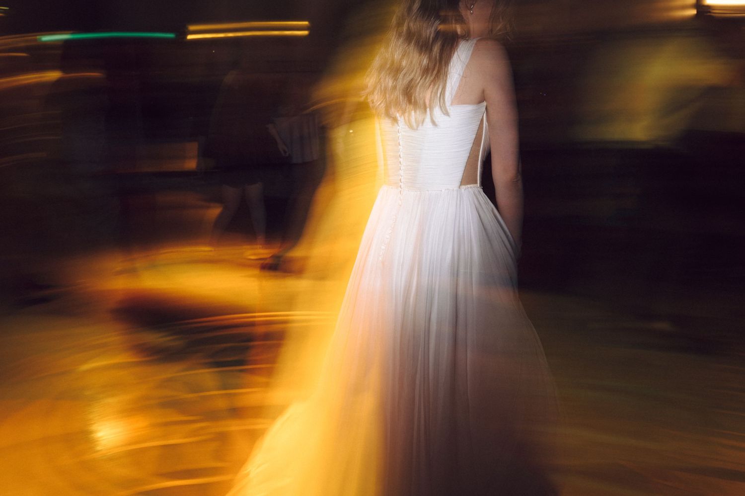 Motion-blurred dancers create glowing streaks of light against dark background at wedding reception.