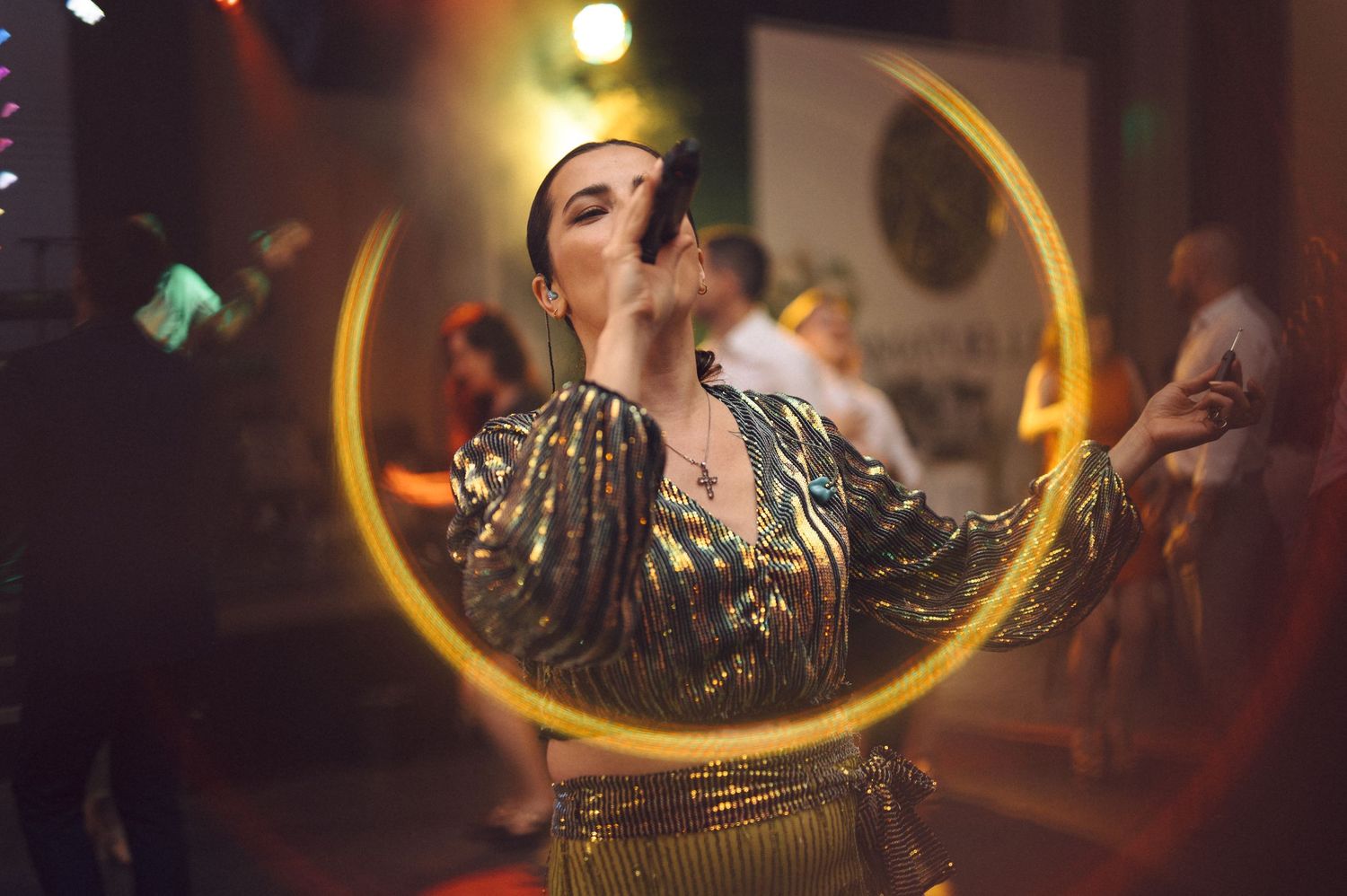 Performer in sequined costume dancing in front of illuminated golden crescent moon backdrop.