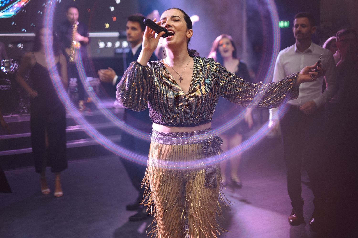 A performer singing on stage in a sparkly outfit with dramatic lighting effects.