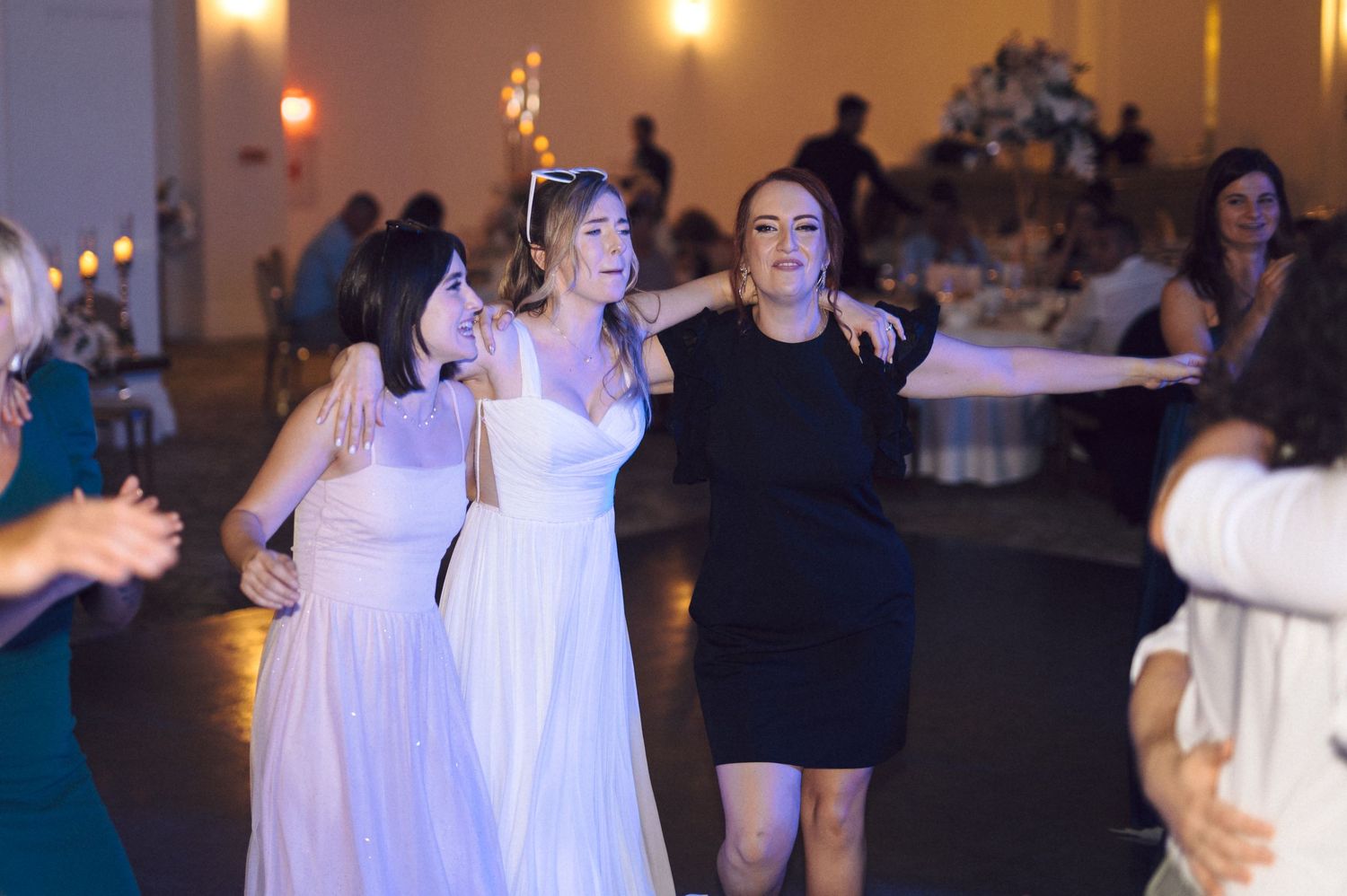 Wedding guests dance and celebrate together on a dimly lit dance floor at a reception party.