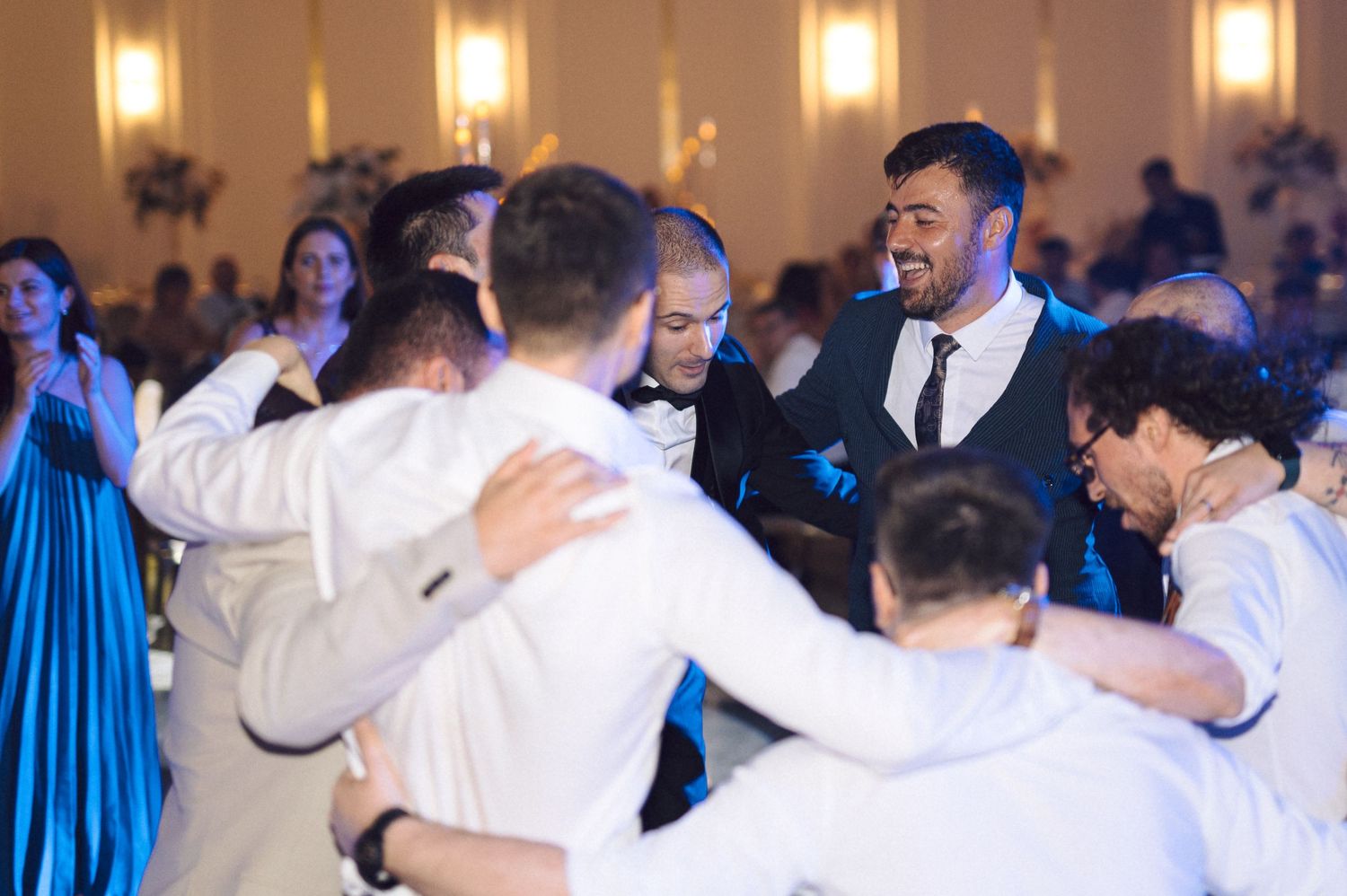 Wedding guests link arms and dance together in a circle during a joyful reception celebration.
