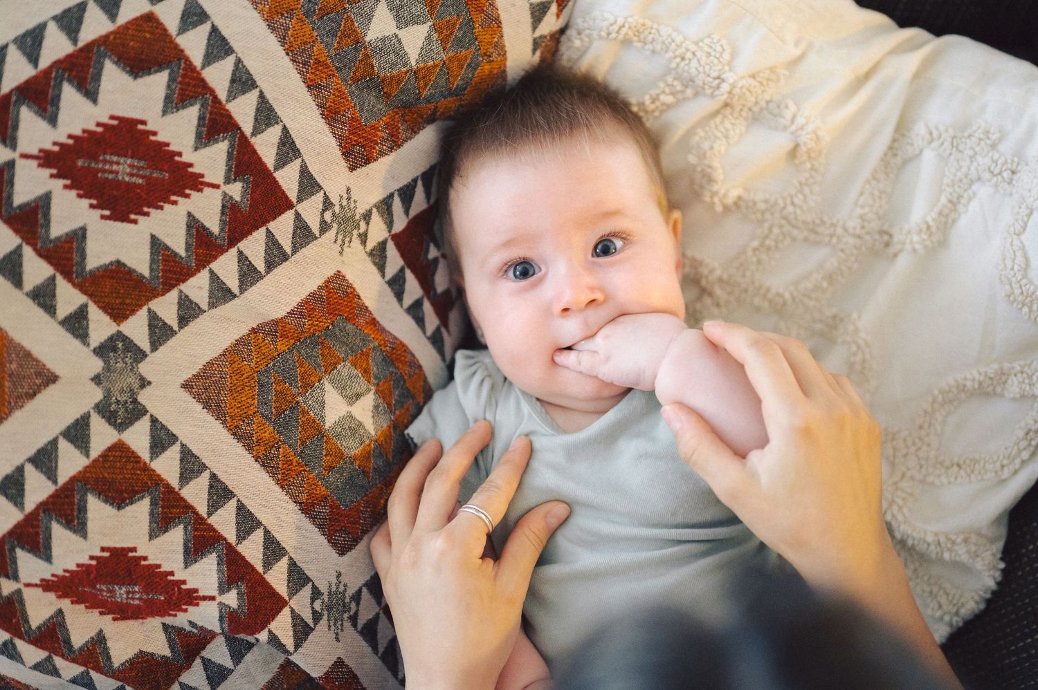 Baby wearing gray onesie lying on blanket with geometric southwestern pattern in orange and brown tones.