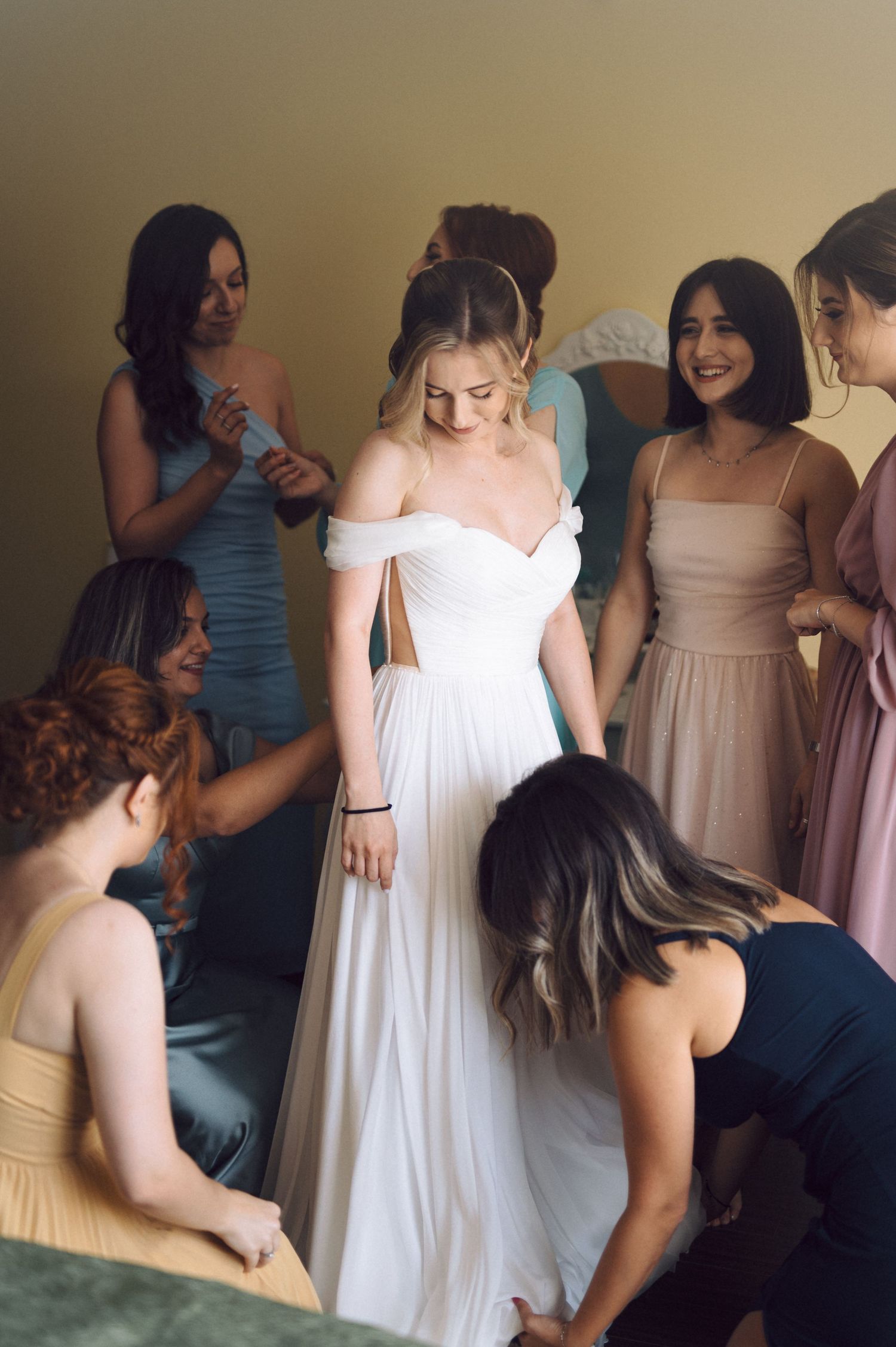 A row of bridesmaids in pastel dresses help prepare before a wedding ceremony.