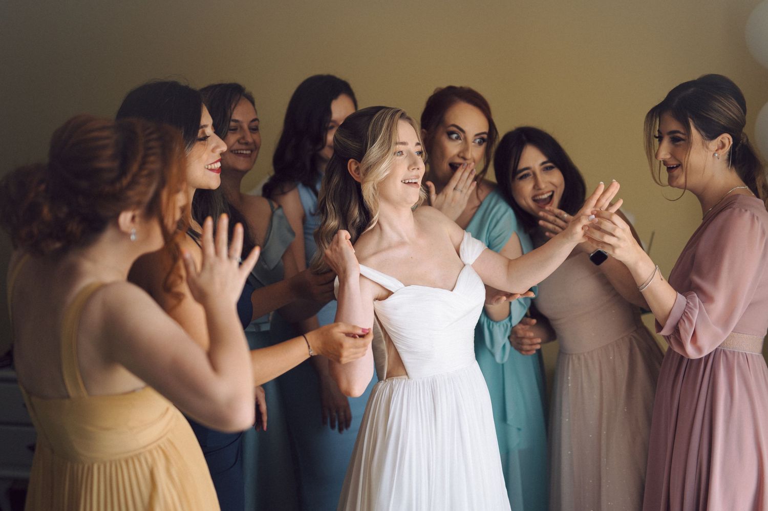 Group of bridesmaids in pastel dresses share laughter and joy during a wedding celebration.