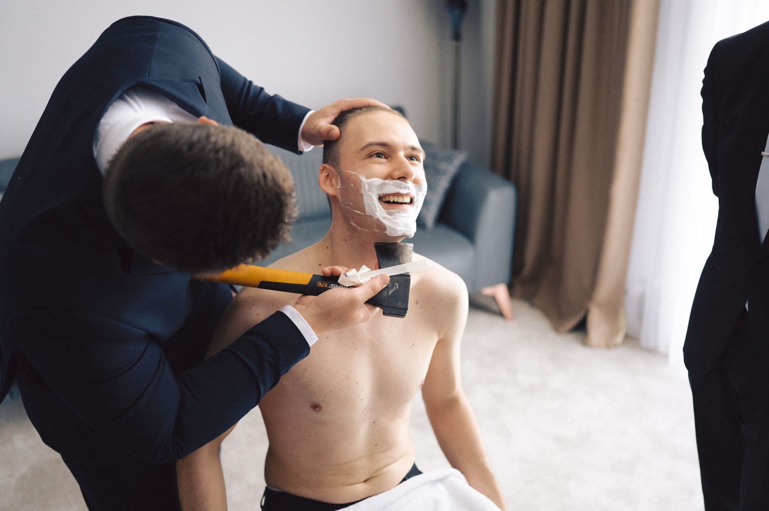 Hairstylist applying grooming products to laughing shirtless man while preparing for a special event.