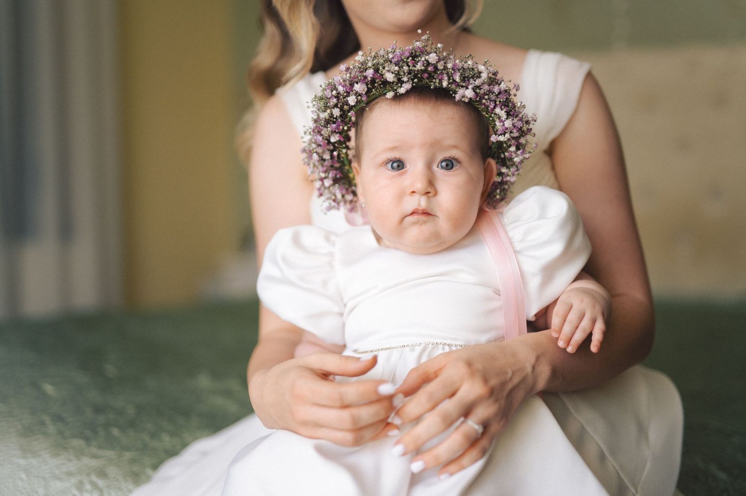 Baby wearing a white tulle dress while being held in someone's arms near a railing.