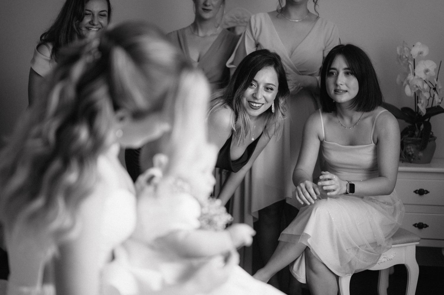 Black and white candid shot of a bridal party sharing a joyful moment during wedding preparations indoors.