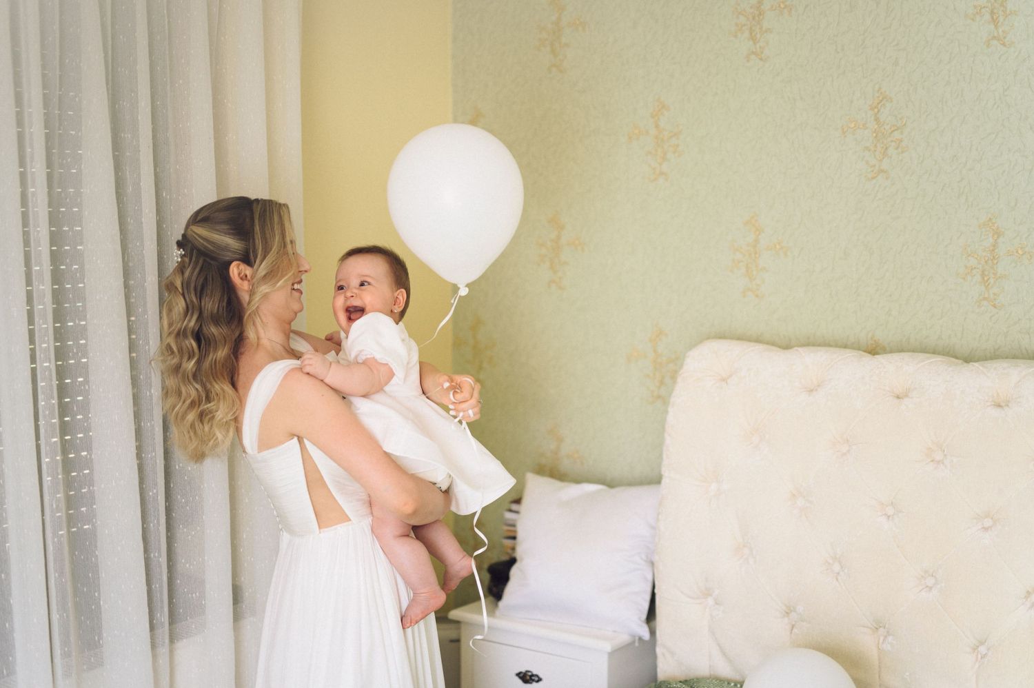 Wedding photographer captures candid moments of bride and bridesmaid preparing and embracing in natural light.