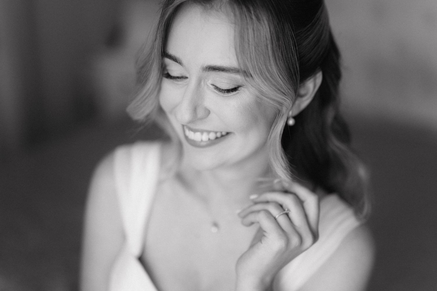 Black and white portrait of a smiling bride wearing earrings with natural makeup and elegant hairstyle.