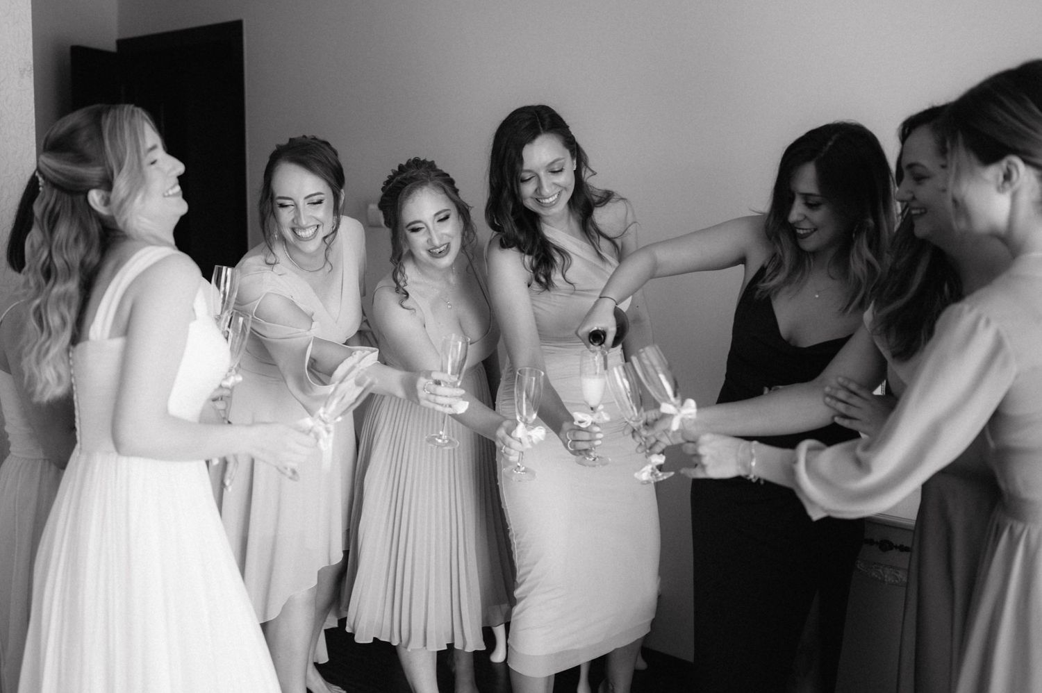 A group in light colored dresses gathers together in celebration, sharing joyful laughter in black and white photography.