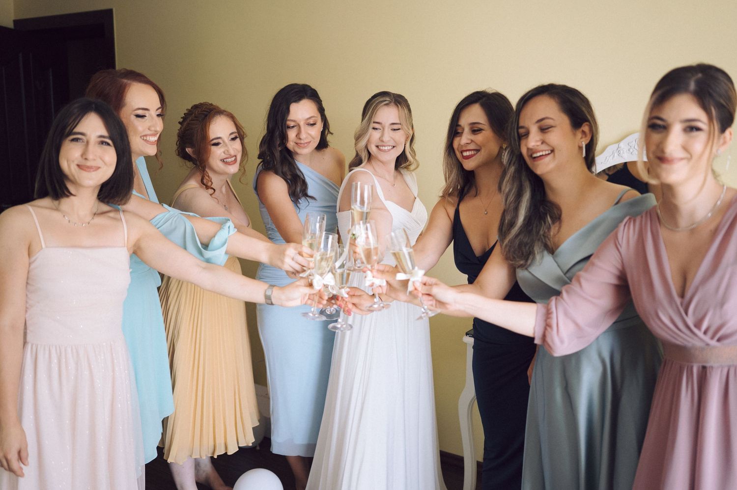 Bridesmaids in pastel dresses toasting with champagne glasses at a wedding celebration.